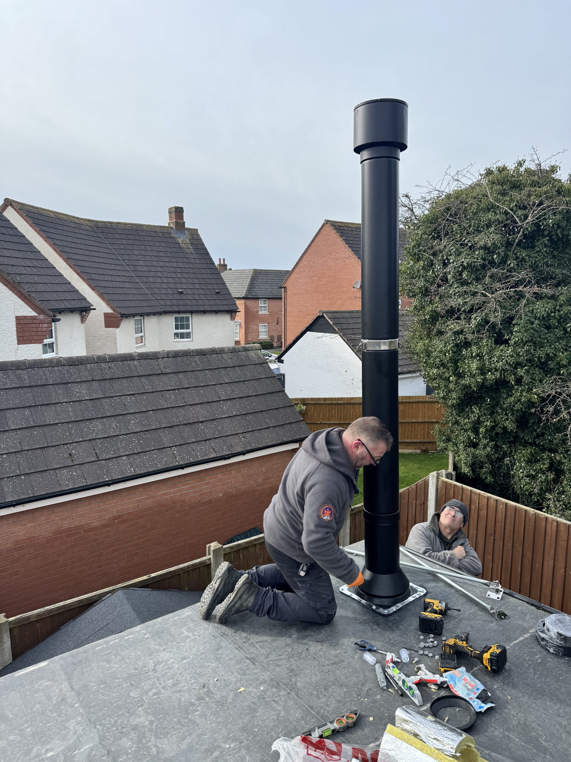Fitting a black twinwall flue through the flat roof of an extension